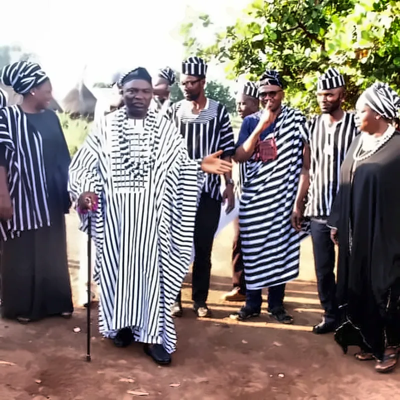 An elder holding a staff walks with members in black-and-white A’nger cloth